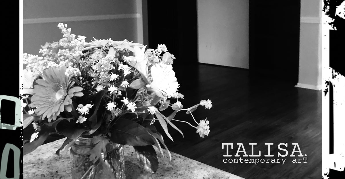 Black and white original photograph of a fresh floral arrangement in a glass jar on a table, blank wall space in background, with the text 'TALISA contemporary art' in the lower right corner.